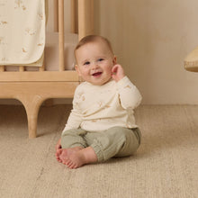 Load image into Gallery viewer, Baby sitting on the floor in a nursery with a crib in the background
