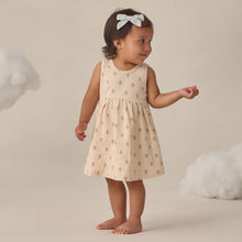 Load image into Gallery viewer, Young child in a beige dress standing against a neutral background with white clouds.