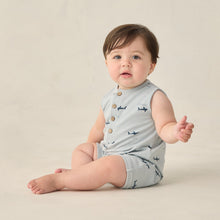Load image into Gallery viewer, Baby wearing a light blue sleeveless romper with button details and airplane pattern on a beige background