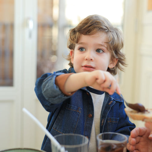 Child sitting at a table with cups and a spoon, looking up