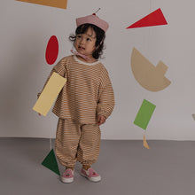 Load image into Gallery viewer, Child in a striped outfit standing in front of a wall with colorful geometric shapes.
