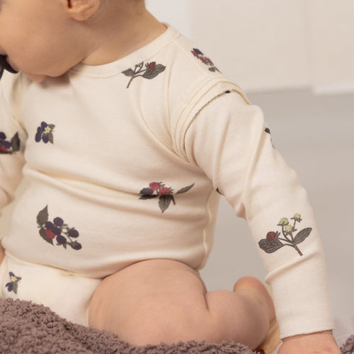 Baby wearing a white long-sleeve shirt with floral patterns on a neutral background