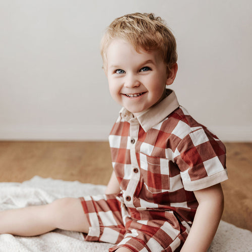 Child wearing a red and white checkered outfit sitting on a blanket.