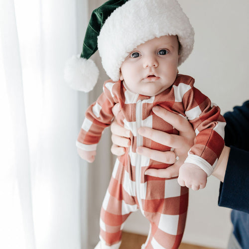 Baby in a red and white striped outfit with a Santa hat being held indoors.