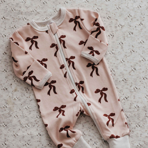 Pink baby onesie with brown patterns on a textured surface