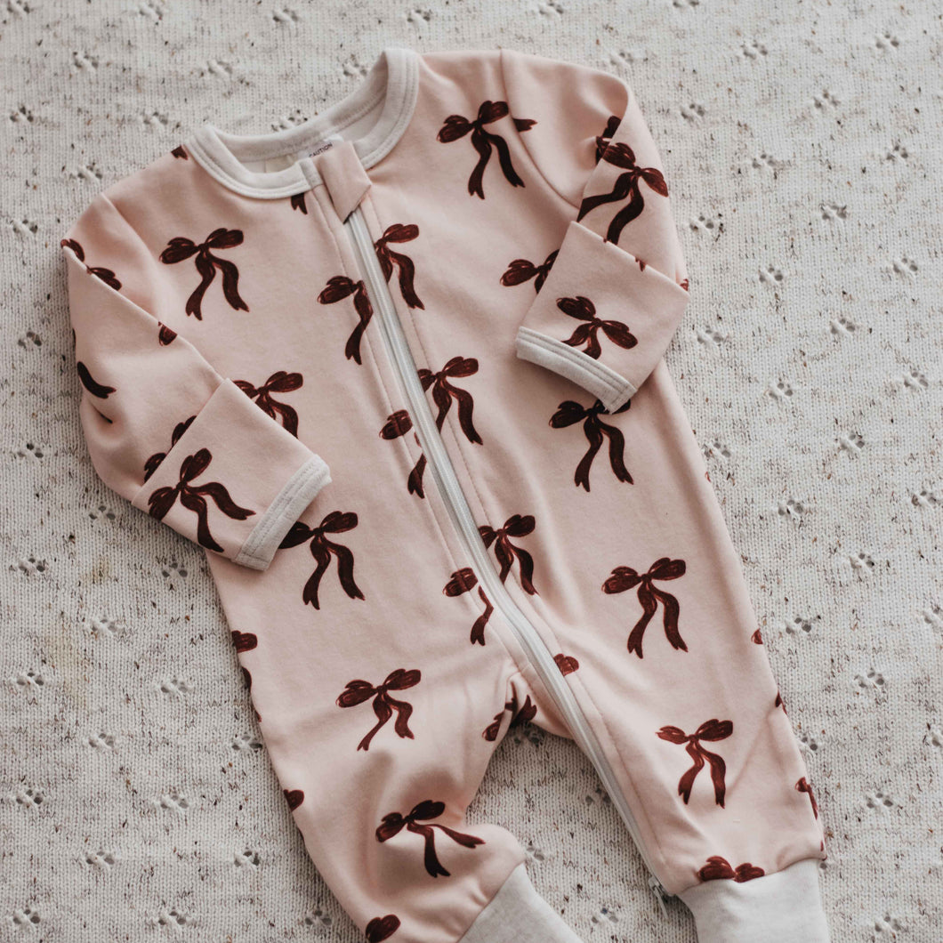 Pink baby onesie with brown patterns on a textured surface
