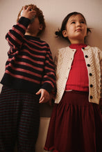Load image into Gallery viewer, Two children standing against a plain wall, one wearing a striped sweater and the other in a red top with a white cardigan.
