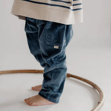 Load image into Gallery viewer, Child wearing a striped shirt and blue corduroy pants standing on a white surface with a wooden ring.
