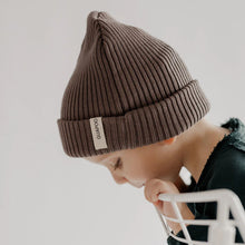 Load image into Gallery viewer, Child wearing a brown beanie with a brand label on a light gray background
