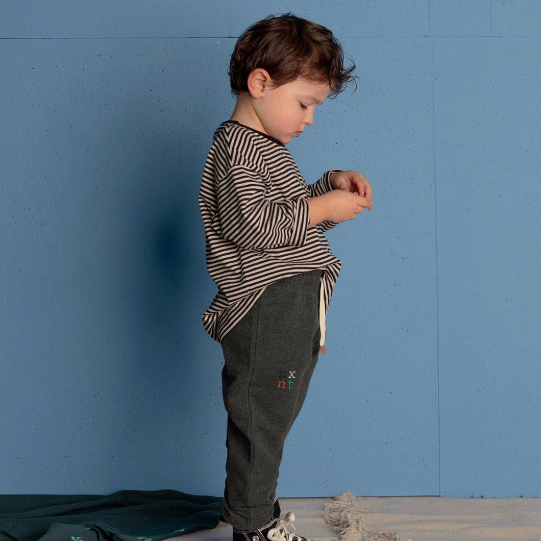 Child wearing a striped shirt and dark pants against a blue wall