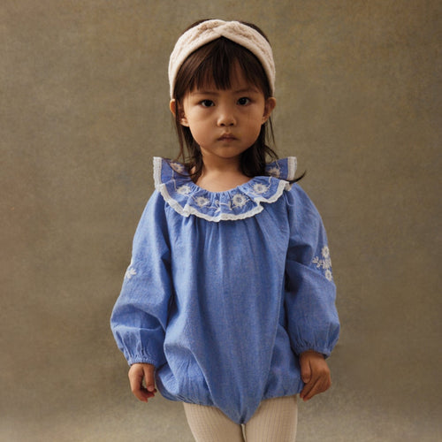 Young girl wearing a blue blouse with lace collar and white tights against a brown background