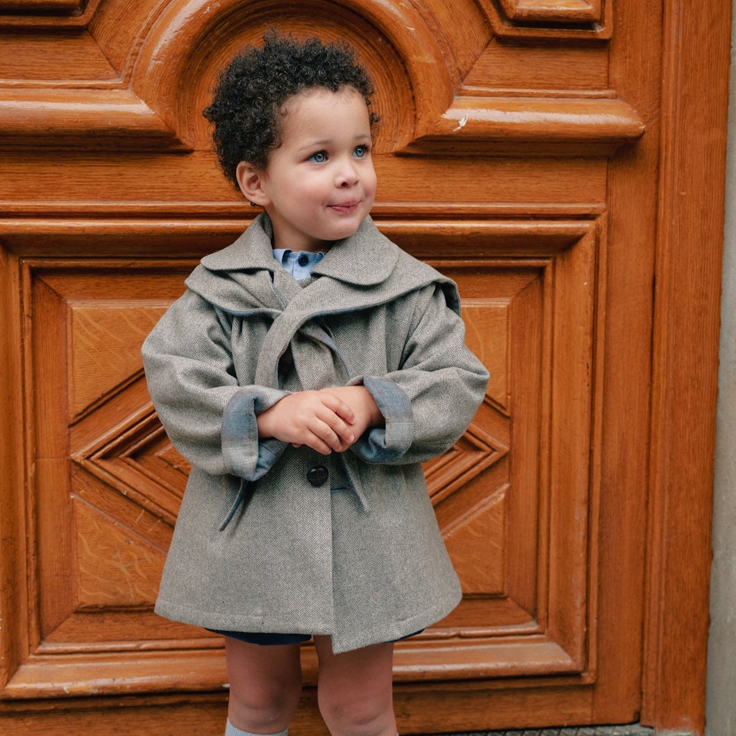 Child in a gray coat standing in front of a wooden door