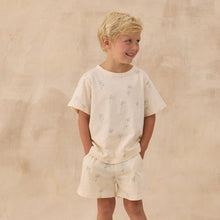 Load image into Gallery viewer, Young boy wearing a white outfit with small patterns against a beige background
