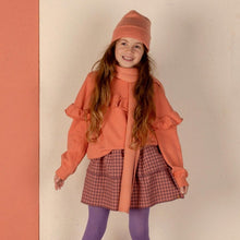 Load image into Gallery viewer, Young girl in an orange outfit standing against a colorful wall.
