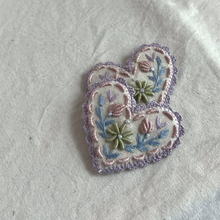 Load image into Gallery viewer, Two small embroidered heart-shaped patches with floral details in pastel purple, pink, blue, and green, placed on a light fabric background.
