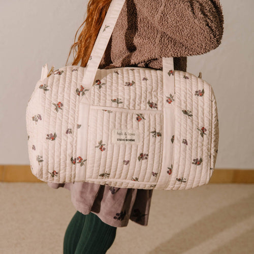 Person holding a large quilted bag with floral pattern on a neutral background