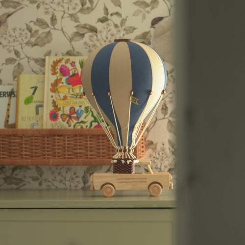 Decorative hot air balloon model on a wooden truck against a floral wallpaper background